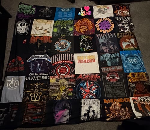 Customer's large Premium T Shirt Quilt made from dozens of music band and concert t-shirts with black fleece, spread on a floor.