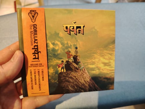 Customer holding the Gorillaz 'The Mountain' Deluxe CD, showing the album's illustrated cover and orange obi strip.