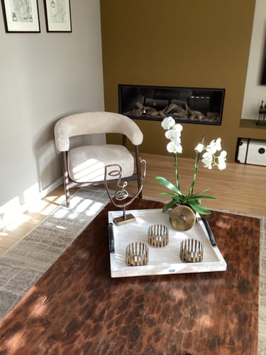 Recensent toont de beige Sora Fauteuil in een zonnige hoek naast een haard.