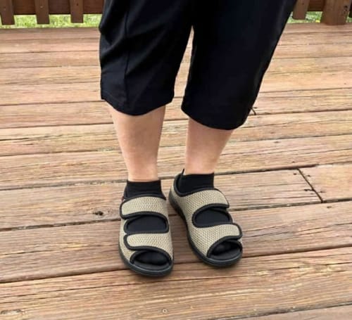 A customer stands on a deck wearing the beige Care Guard sandals with black socks, showing the fit and adjustable straps.