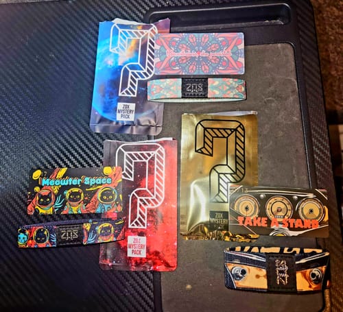 Customer displays three varied straps and their foil packaging from a Non-Interactive Mystery 3-Pack.