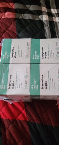 Customer's multi-pack of Everywhere Wipes in shrink wrap, resting on a plaid comforter.