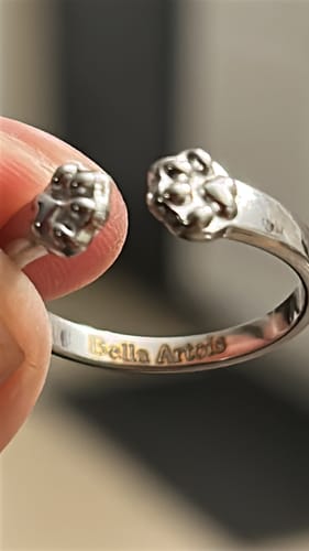 Close-up of the Paw Hug Ring held by a reviewer, showing the personalized engraving 'Bella Artois' on the inside.