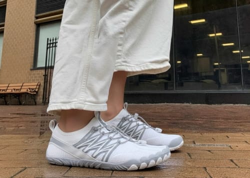 Reviewer wearing the white and grey BareEase shoes on a wet sidewalk, showing their flexible design.