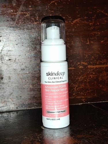 Customer's white pump bottle of Advanced PDRN Skin Repair Serum on a wooden surface.