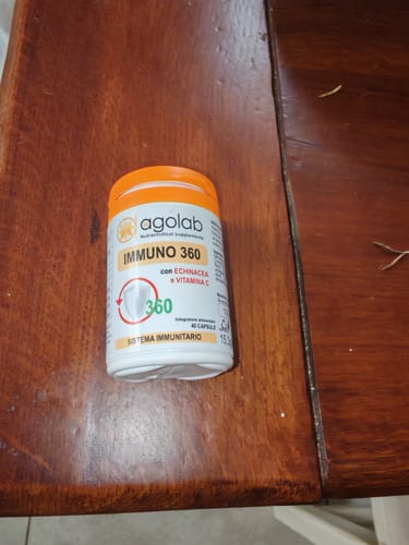 Recensore mostra il flacone di Immuno 360 su un tavolo di legno.