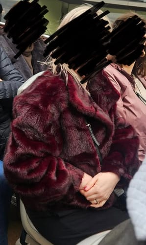 Customer sitting while wearing the burgundy Faux Fur Jacket, showing its thick, plush material.