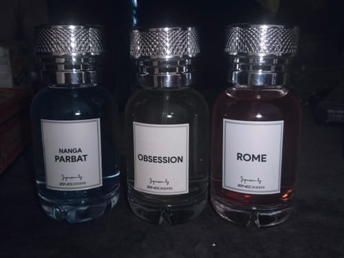 Reviewer's three assorted oud perfume bottles with silver caps lined up on a dark surface.