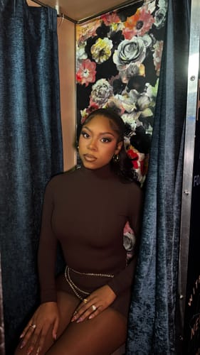 Close-up of a customer in a photo booth wearing the brown Butter Turtleneck Contour Bodysuit with a delicate chain belt.