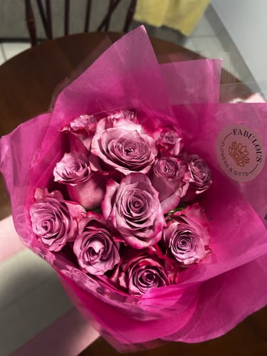 Customer's overhead view of the Dusty Pink Rose Bouquet wrapped in vibrant pink paper on a table.