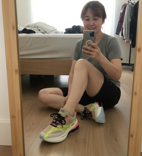 Reviewer takes a mirror selfie while sitting on the floor wearing colorful Cloud Walk sneakers.