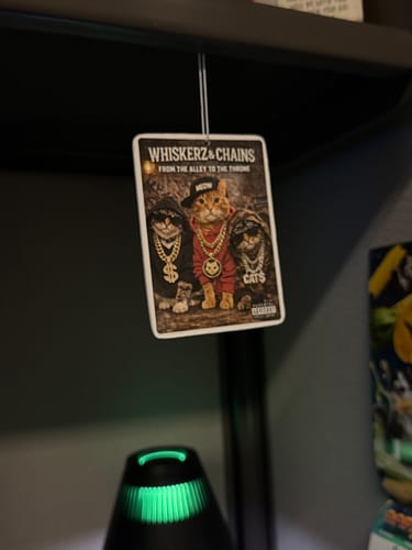 Customer's custom air freshener hanging indoors, printed with a funny graphic of three cats in hip-hop gear.