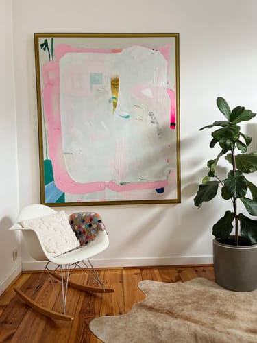 Recensent toont het HKliving White Sands schilderij met olijfkleurige lijst, hangend aan de muur boven een schommelstoel.