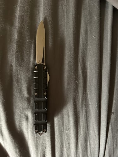 A customer's black VT Workman Utility Switchblade shown fully open on a dark striped surface.