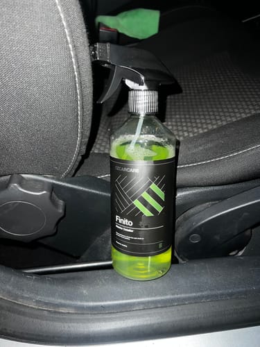 Reviewer's bottle of Finito Interior Detailer, containing a bright green liquid, placed inside a car next to the seat.