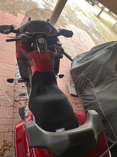 A reviewer's red motorcycle from a high angle, showing the black mesh Wind Rider Seat Cover installed on the seat.