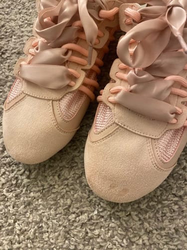 Reviewer's pair of pink SHERYL sneakers on a carpet, showing a small defect on the suede toe.