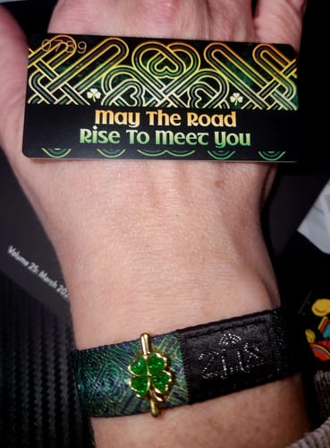 Customer's hand wearing the green May The Road Rise To Meet You Bracelet with its matching collector's card.