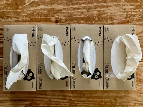Photo d'un client montrant quatre boîtes de mouchoirs en carton posées côte à côte sur une table en bois.