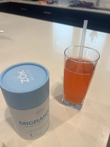 Customer's container of Migranium next to a prepared glass of the Berry Bliss drink.