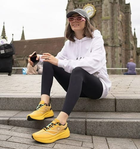 Reviewer sitting on outdoor steps, wearing bright yellow Cloud Walk shoes with leggings and a hoodie.