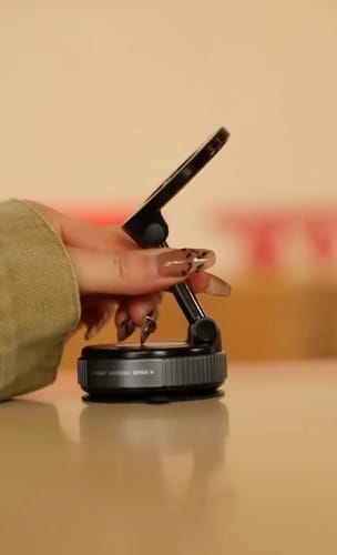 A reviewer's hand adjusting the 360° MagPro Magnetic Phone Holder with a phone attached, set on a smooth, flat surface.