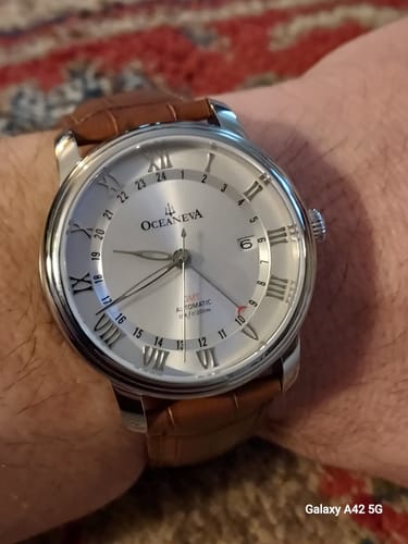 Close-up of the Oceaneva OceanTrek watch on a reviewer's wrist, showing its silver dial and brown leather strap.