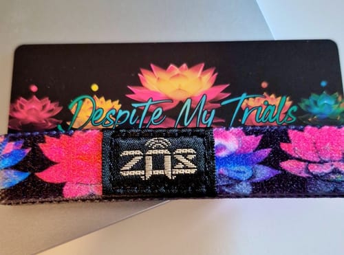 Close-up of a customer's colorful 'Despite My Trials' bracelet with a lotus pattern, shown with its themed backing card.