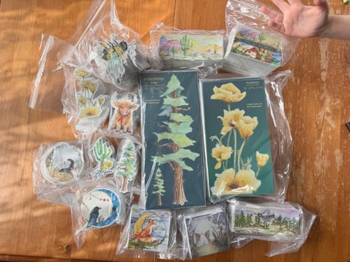 Reviewer's collection of custom vinyl stickers with beautiful watercolor designs of plants and animals laid out on a wooden table.