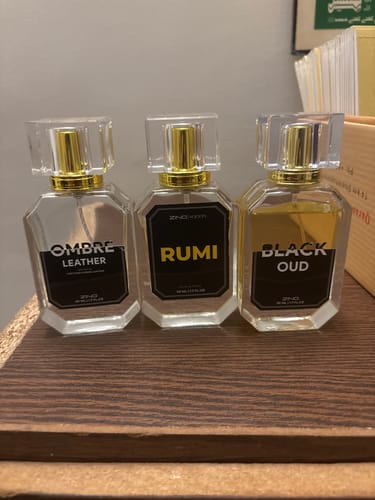Customer's three OUD Supreme BUNDLE perfume bottles with clear caps and gold details lined up on a wooden shelf.