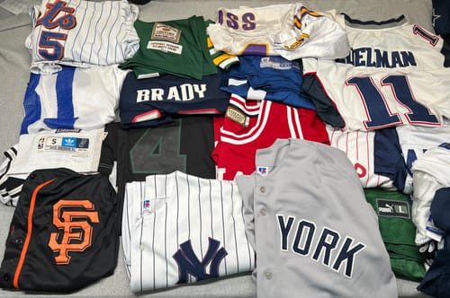 Customer's assortment of pro and college sports jerseys laid out, showing teams like the Yankees, Patriots, and Giants.