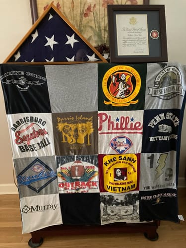 Customer's memorial Project Repat T-Shirt Quilt with military and college shirts, displayed below a folded flag.