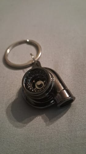 A reviewer's dark metallic Turbo Keychain resting on a grey textured surface.
