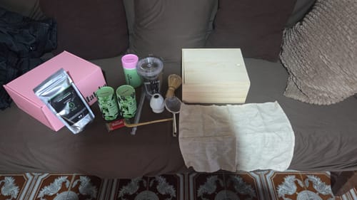 Un cliente muestra su Té Matcha Premium y varios accesorios sobre un sofá, incluyendo cajas y utensilios.