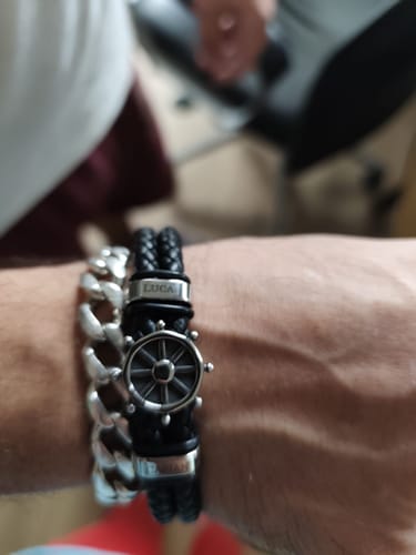 Close-up of a reviewer's wrist wearing the black braided Captain bracelet, showing the ship's wheel and a personalized bead.