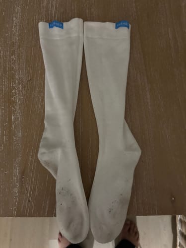 Customer's pair of white Performance Eucalyptus Compression Socks laid out on a wood surface, showing dirty soles.