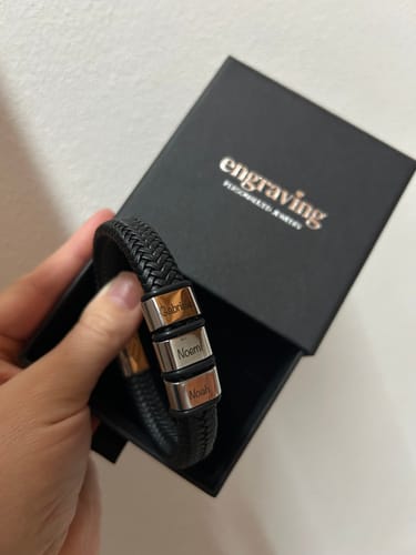 A customer's hand holding a black braided Viking bracelet with three engraved silver beads over its open gift box.