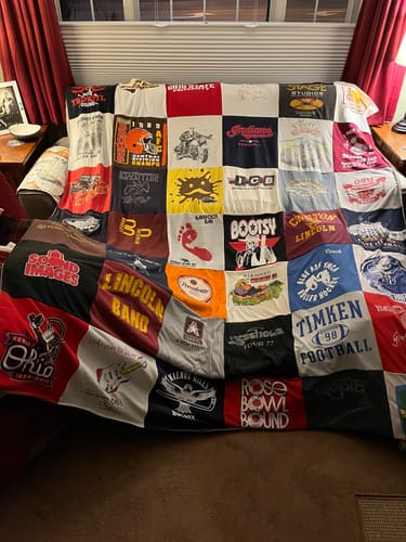 Customer's large, colorful Premium T Shirt Quilt, made from many t-shirts, draped over the back of a couch.