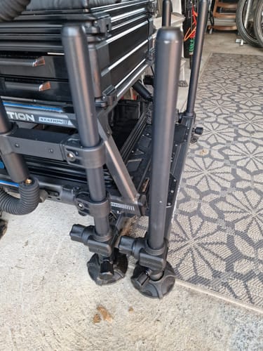 Recensent toont de zwarte Inception 30mm poten, gemonteerd op een viskist, met de moddervoeten zichtbaar.