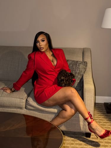 Reviewer sitting on a couch wearing the red Suiting Blazer Mini Dress, paired with red heels and holding a furry clutch.