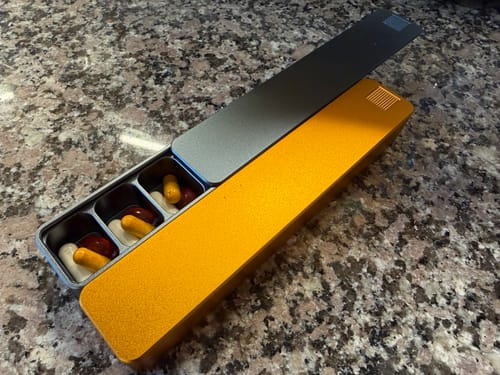 Customer's open Weekly AM-PM Pill Case 2.0 on a granite counter, showing pills in its metal compartments.