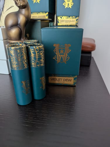 Customer's Violet Dew perfume with its teal and gold box and two matching travel sprays on a desk.