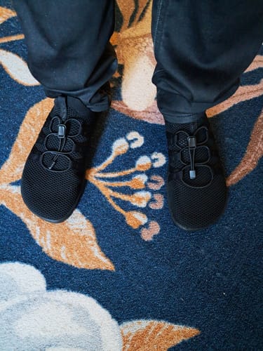 Asiakkaan jalassa mustat Vaistoa Riemu -paljasjalkakengät kuviollisella matolla.