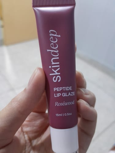 Customer holding the mauve-colored tube of Skindeep Peptide Lip Glaze in the shade Roséwood.
