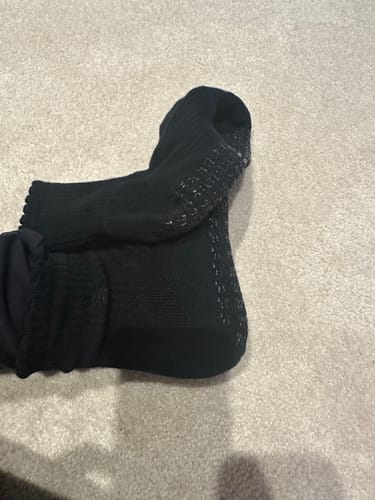 Close-up of a reviewer's foot in a black Dual-Direction Grip Basics sock, showing the grips on the sole.