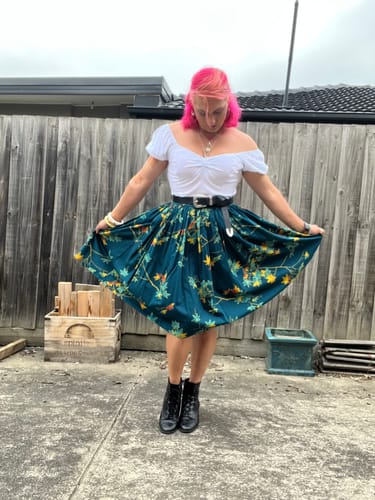 Customer wearing the white Powder Puff Top with a full patterned skirt and black boots in a backyard.