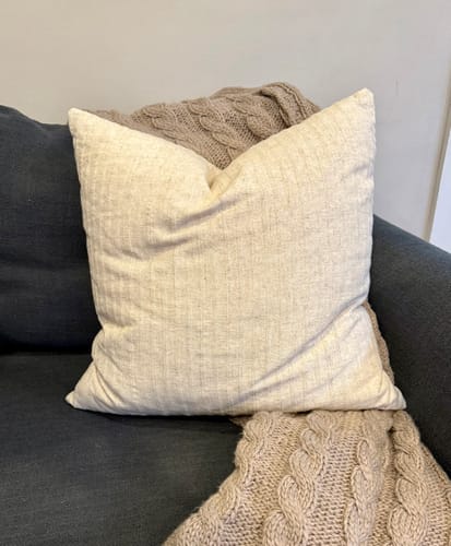 Customer's cream, textured Mabel pillow cover styled with a chop on a dark sofa.