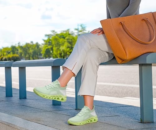 Customer sitting on an outdoor bench wearing light green Ortho Step sneakers with casual pants.
