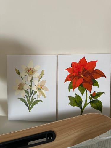 Reviewer displays two completed mini paintings from the set: one with white lilies and another with a red poinsettia.