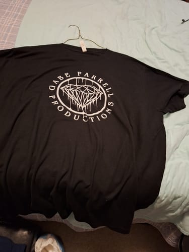 Customer's black Drip Tee with a white graphic print laid out on a bed.